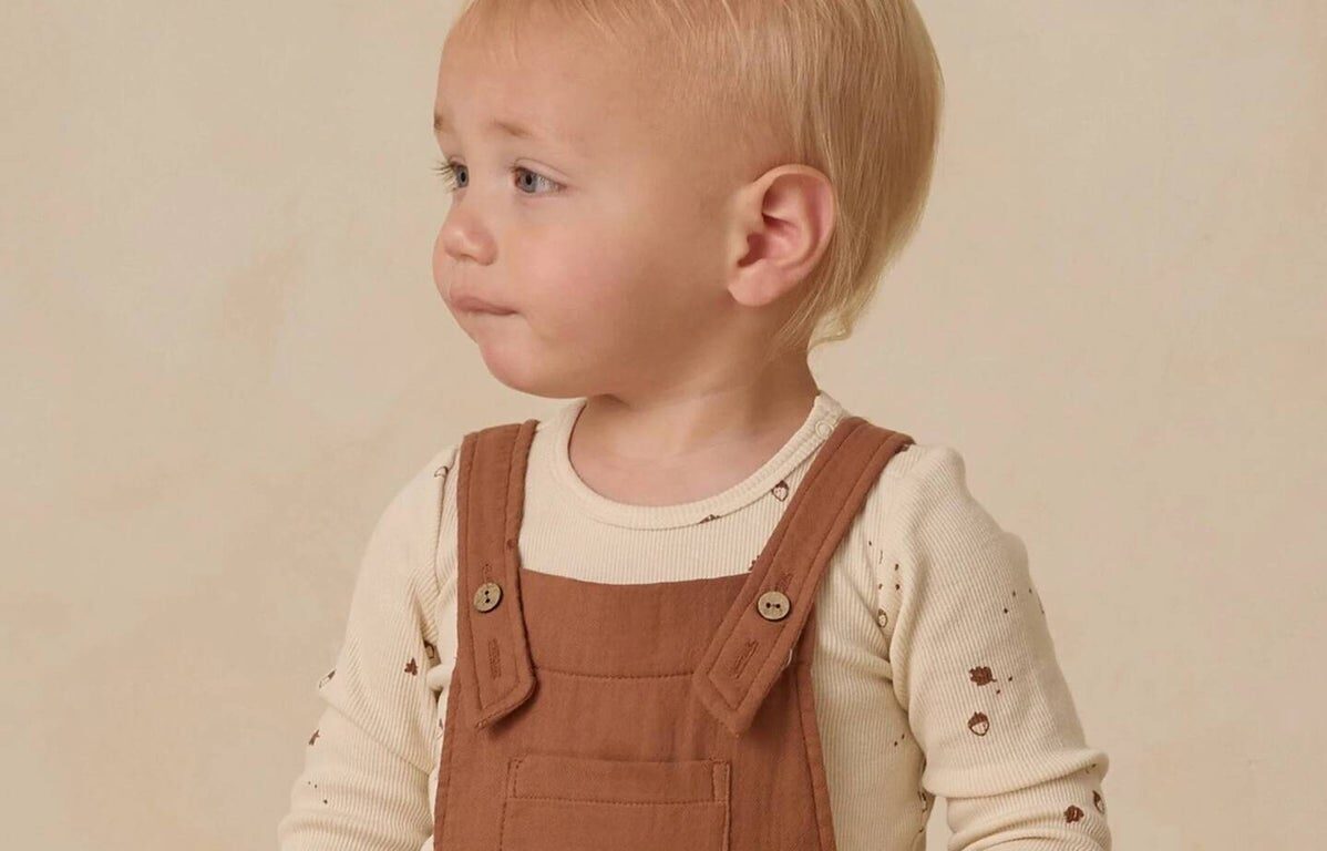 Toddler in brown overalls looks sideways.