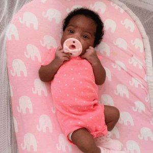 Baby in pink outfit with pacifier, elephant bedding.
