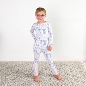 Child wearing bow-patterned pajamas standing on rug.