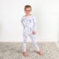 Child wearing bow-patterned pajamas standing on rug.