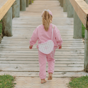 Toddler in pink outfit walking on wooden pathway.