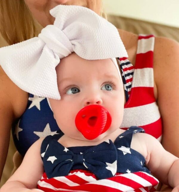 itzy ritzy sweetie soother™ pacifier sets (2 pack): agave + succulent cables Baby in patriotic outfit with large white bow.