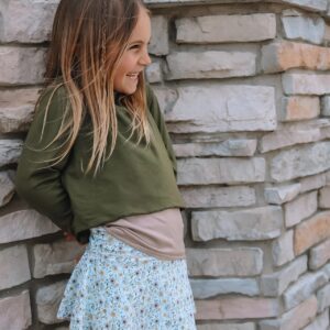 Smiling child leaning against stone wall, floral skirt.