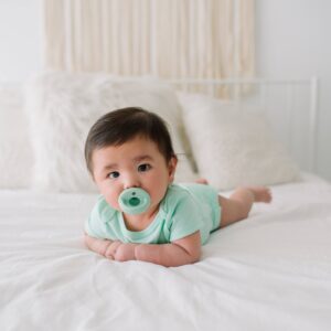 Baby lying down with a green pacifier