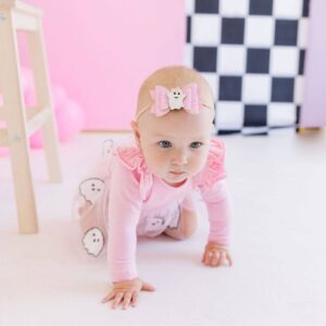 Baby in pink crawling with ghost-themed outfit.