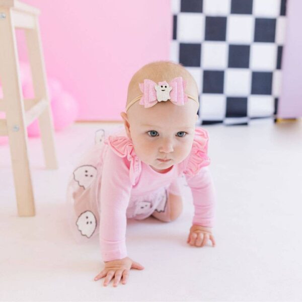 Baby in pink crawling with ghost-themed outfit.