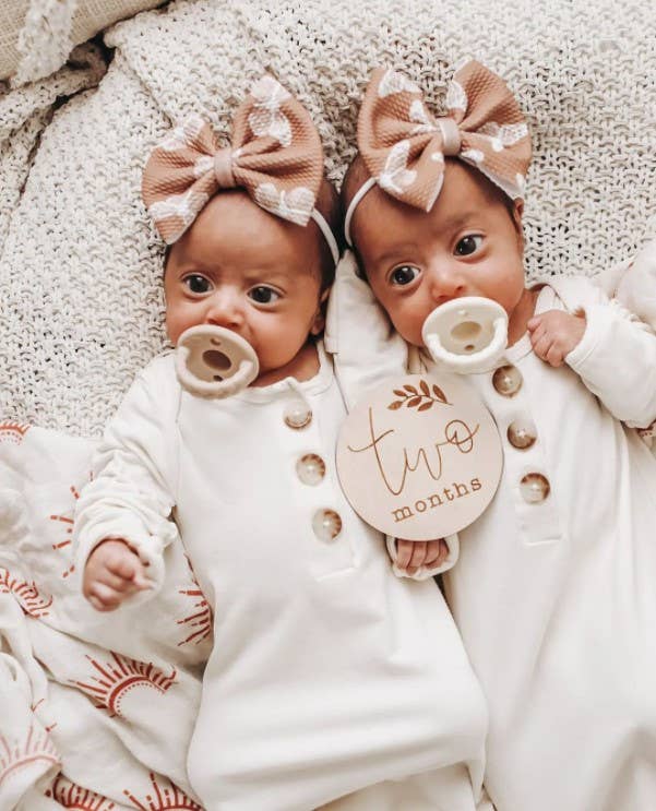 itzy ritzy sweetie soother™ pacifier sets (2 pack): pink bows Two-month-old twins wearing matching outfits and bows.