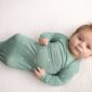 Baby in green swaddle on white blanket