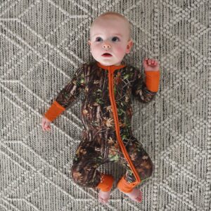 Baby in camouflage pajamas on patterned rug.