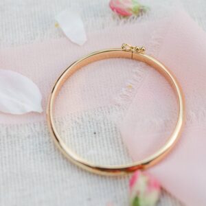 Golden bracelet on pink fabric with flower petals.