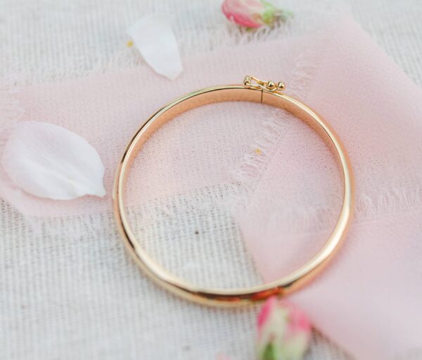 Golden bracelet on pink fabric with flower petals.
