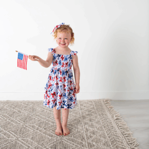 Child holding American flag, wearing star-patterned dress.