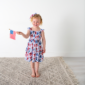 Child holding American flag, wearing star-patterned dress.