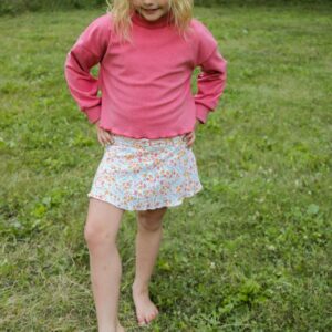 Child outdoors wearing pink sweater and floral skirt.