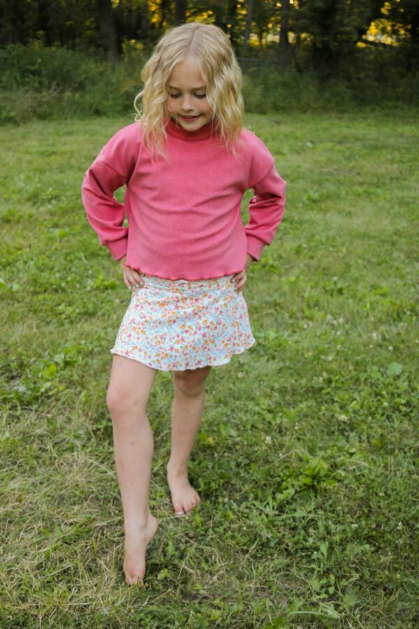 Child outdoors wearing pink sweater and floral skirt.