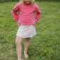 Child outdoors wearing pink sweater and floral skirt.