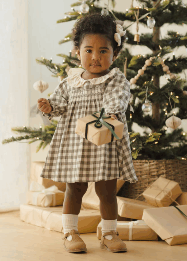 Child with gift near decorated Christmas tree.