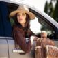 Woman in hat leans from car holding backpack.