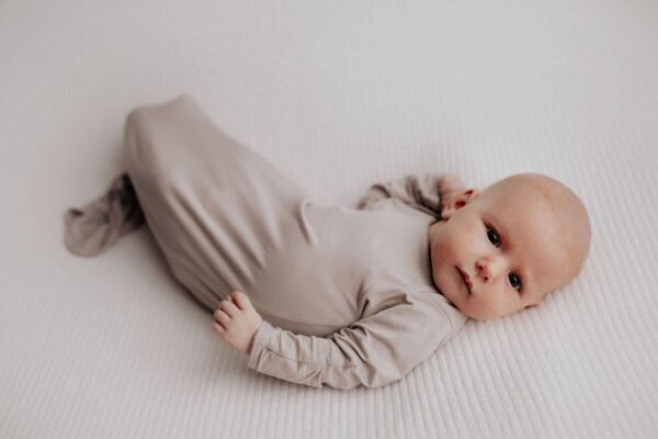 three little tots harbor mist taupe knotted gown Baby lying on a white blanket.