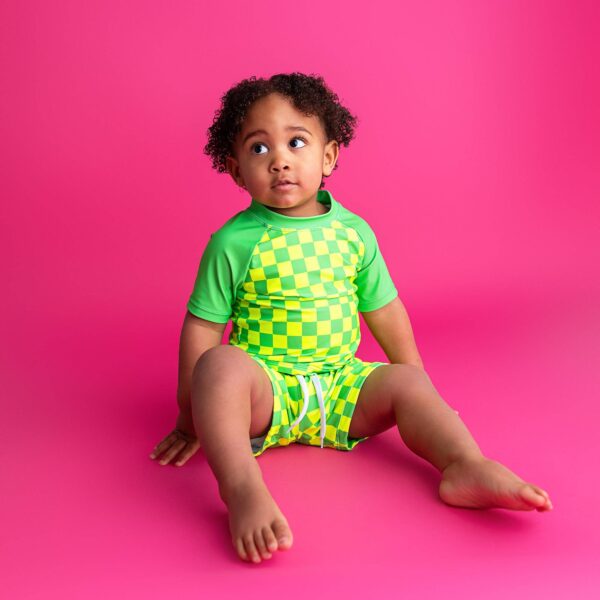 Child in green checkered outfit on pink background.