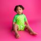 Child in green checkered outfit on pink background.