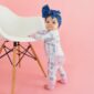 Baby in blue bow standing by chair