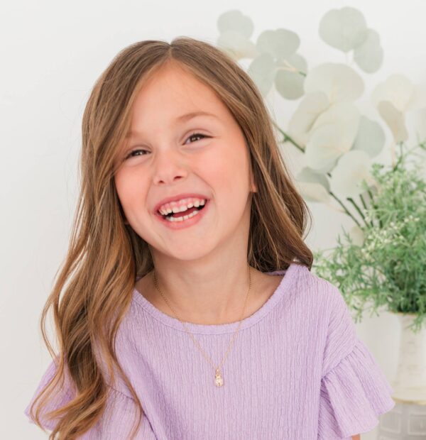 Smiling child in purple dress, green plant background.