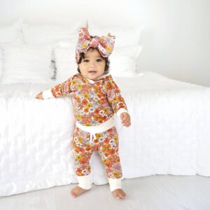 Baby in floral outfit standing by bed