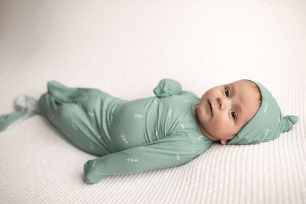 three little tots arrow print knotted newborn baby gown pajamas Baby in green swaddle, lying on white blanket.