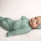 Baby in green swaddle, lying on white blanket.