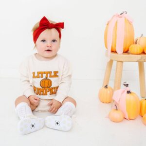 Baby in 'Little Pumpkin' outfit with pumpkins.