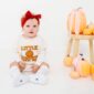 Baby in 'Little Pumpkin' outfit with pumpkins.