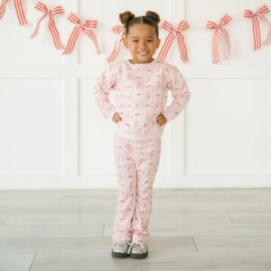 Child in pink pajama set with red bows.