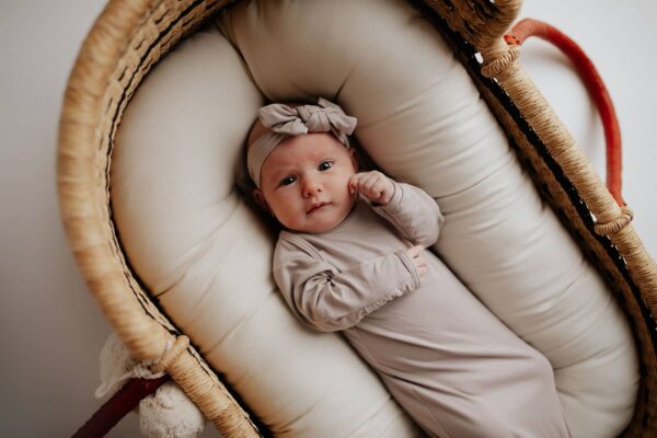 three little tots harbor mist taupe knotted gown Infant in beige outfit lying in basket