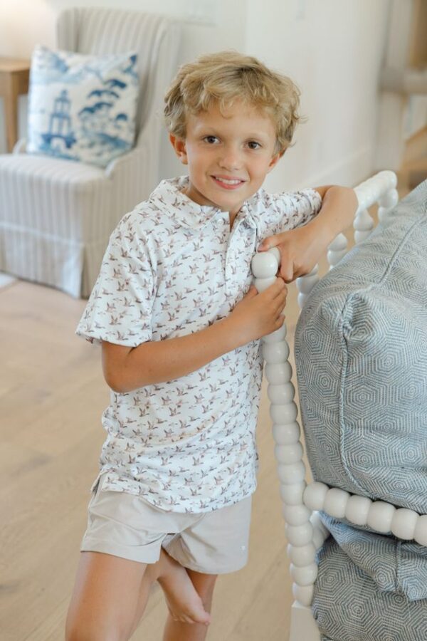 Smiling child stands by bed in bright room.