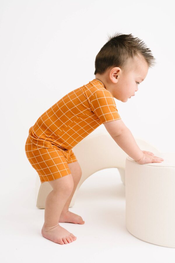 Toddler in orange outfit climbs white furniture.