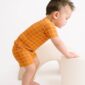 Toddler in orange outfit climbs white furniture.