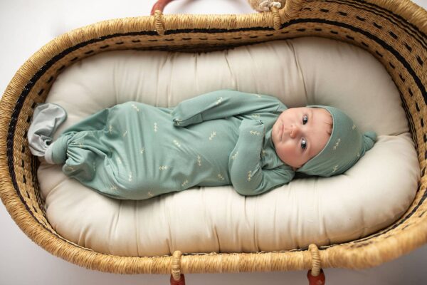 three little tots arrow print knotted newborn baby gown pajamas Baby in green onesie lying in wicker bassinet.