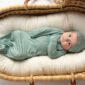 Baby in green onesie lying in wicker bassinet.