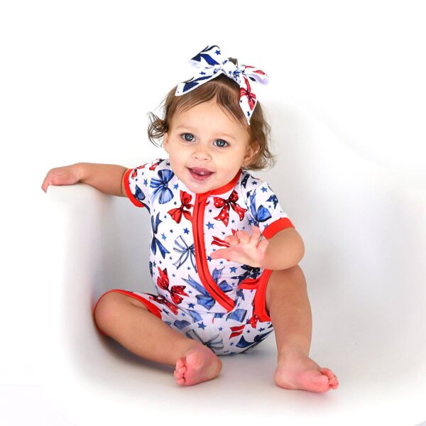 gigi and max eleanor bow clip bow 4th of july hair accessory Smiling baby in colorful patterned outfit and headband.