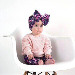 Baby in pink sweater, floral headband on chair.