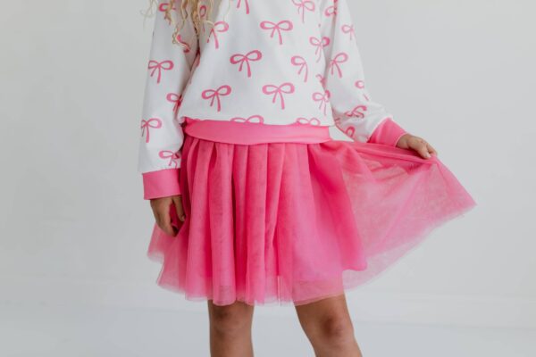 product Child wearing pink skirt and bow-patterned top.