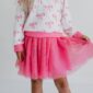 Child wearing pink skirt and bow-patterned top.