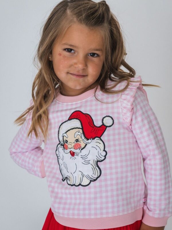 Child wearing Santa-themed sweater, smiling confidently.