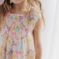 Child wearing colorful, ruffled dress with bows.