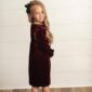 Girl in maroon dress with long hair and bow.