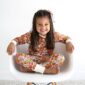 Child smiling in floral pajamas on white chair.