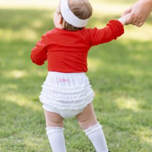 Baby in red shirt holding adult's hand outdoors.