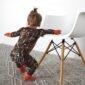 Toddler in camouflage pajamas leans on white chair.