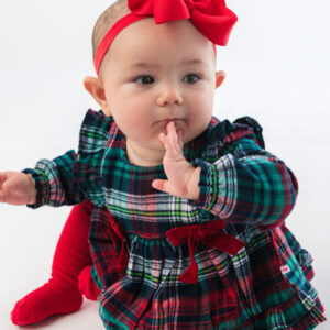 Baby in plaid dress with red bow headband.